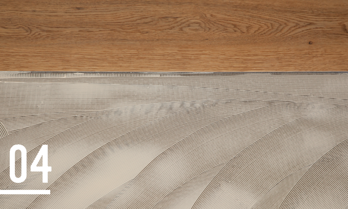 A close-up of a wooden surface at the top and a textured adhesive layer with evenly spaced grooves in the lower part of the image. The grooves form a curved pattern, likely part of a flooring installation process. The number "06" is displayed in bold white font in the bottom left corner.