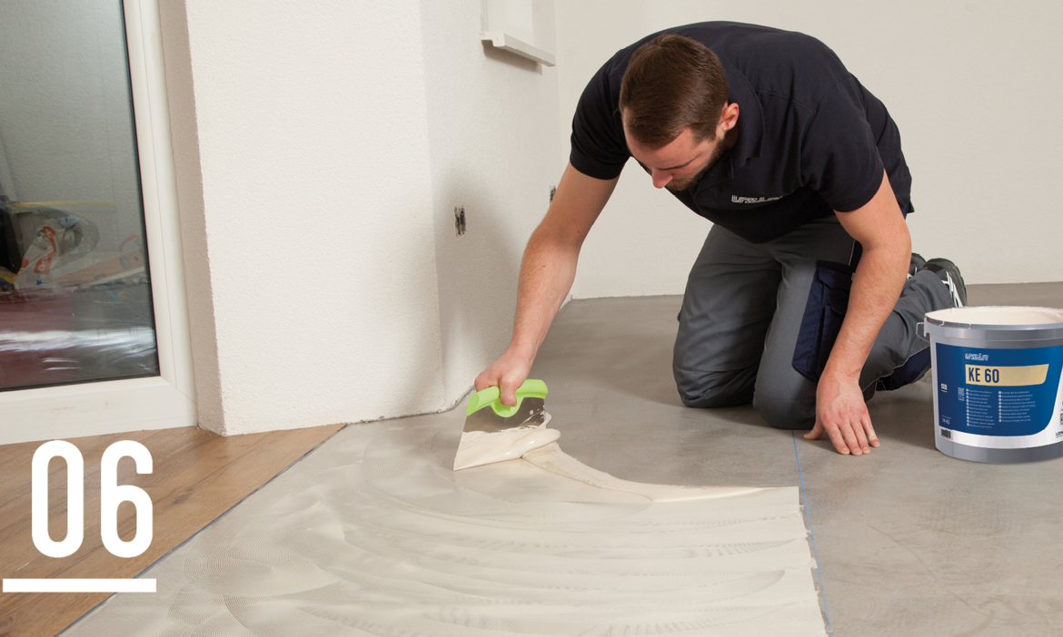 Craftsman applies UZIN KE 60 adhesive for PVC-free floor coverings with a smoothing trowel to a floor covering, sustainable indoor floor installation.